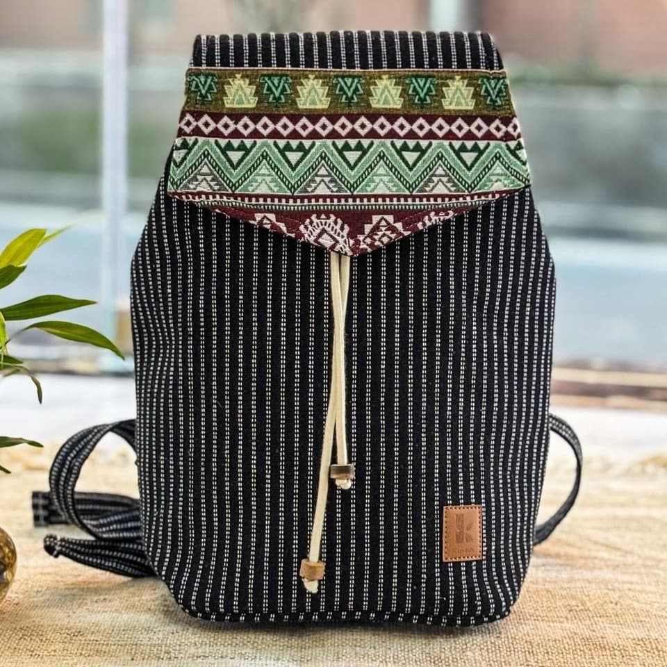 A dark pinstriped hemp backpack with a green and red patterned flap, resting on a wooden table