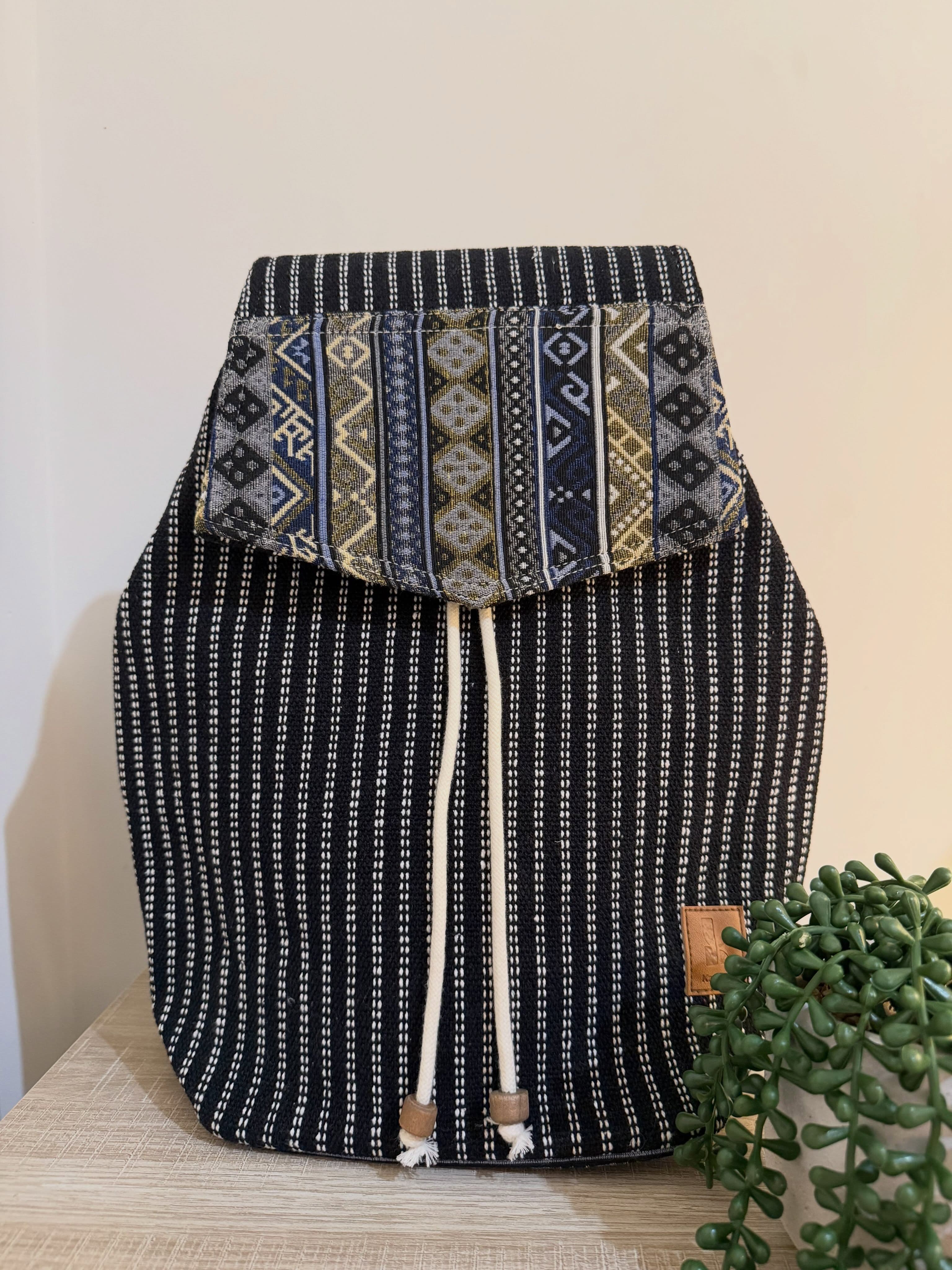 The dark pinstriped hemp backpack in Midnight Indigo under a blue and cream geometric dhaka-patterned flap