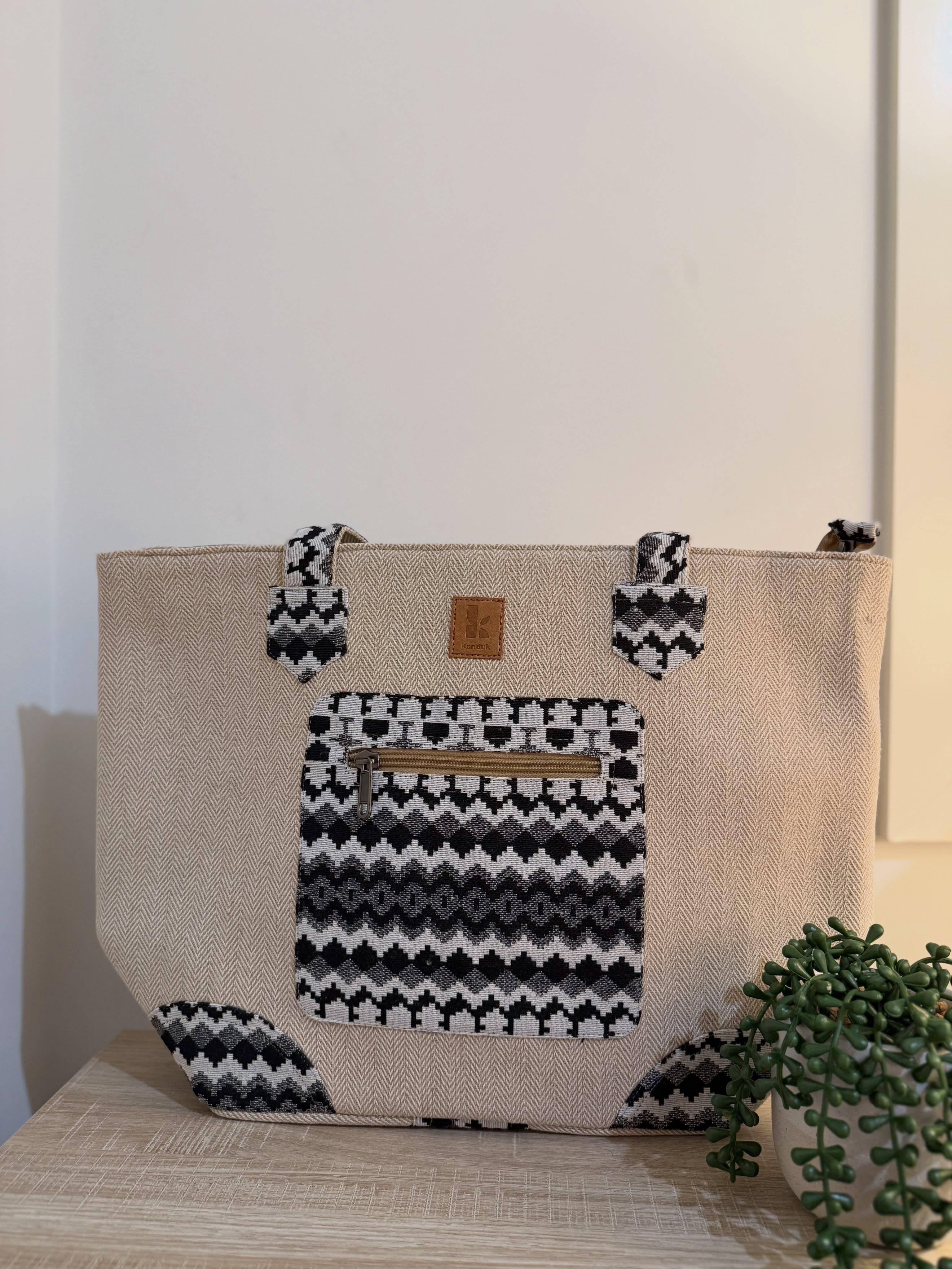A sand-coloured herringbone hemp tote with a black and cream zigzag woven front pocket