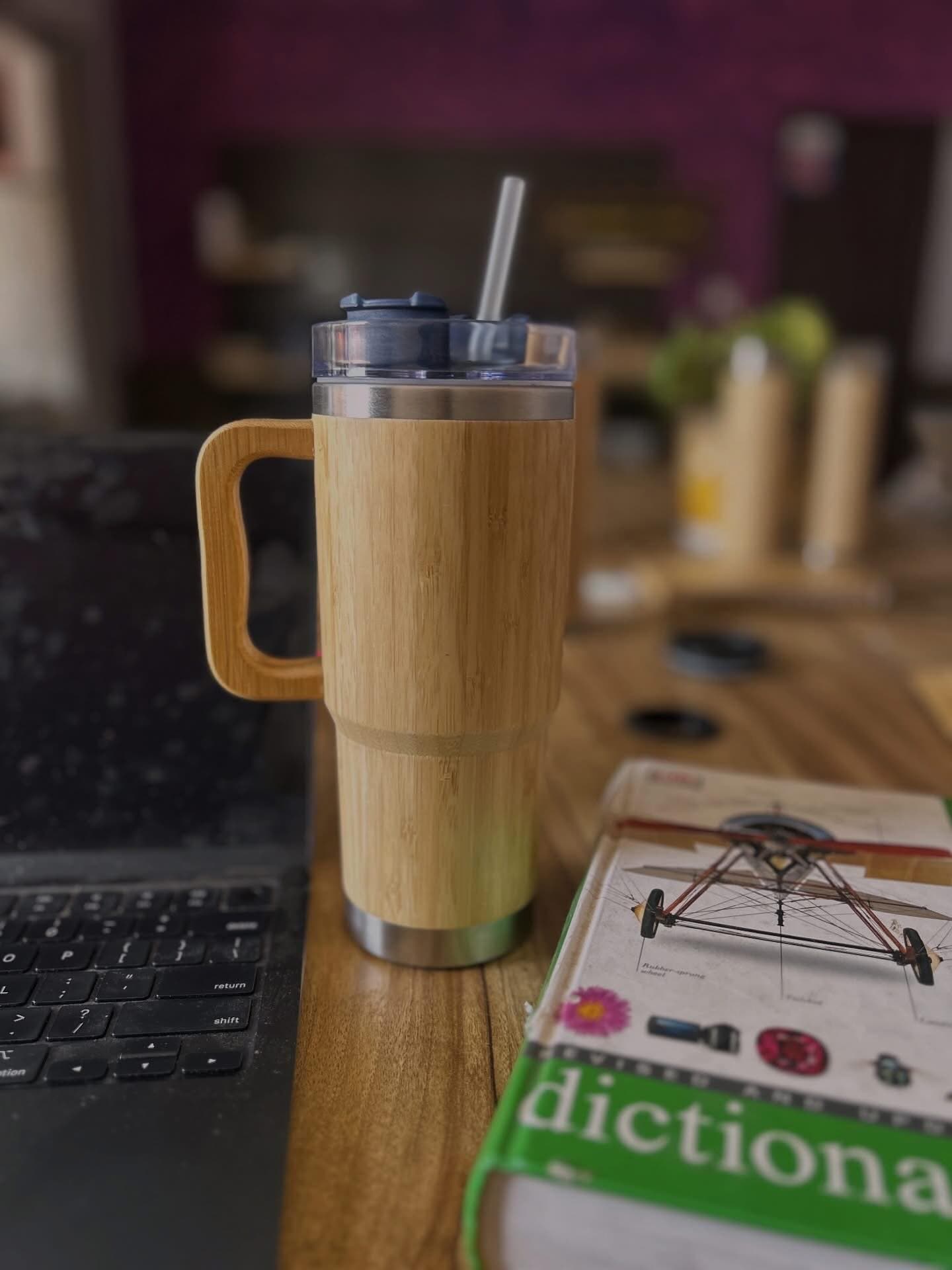 A bamboo-sleeved travel tumbler with a wooden handle and a steel straw, standing on a desk